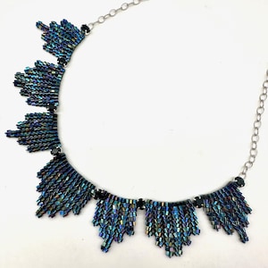 May include: A silver chain necklace with a beaded pendant. The pendant is made of iridescent blue and black beads arranged in a cascading pattern.