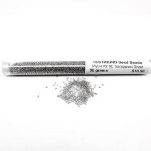 May include: A clear plastic tube filled with small, silver seed beads. The tube has a white label that reads "15/0 ROUND Seed Beads Miyuki #318C Transparent Ghost 30 grams $10.50".