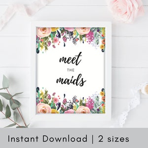 Könnte beinhalten: Ein gerahmter Druck mit dem Text "meet the maids" in schwarzer Schrift, umgeben von einem Aquarell-Blumenrand. Die Blumen sind in Rosa, Gelb und Lila gehalten. Der Rahmen ist weiß.