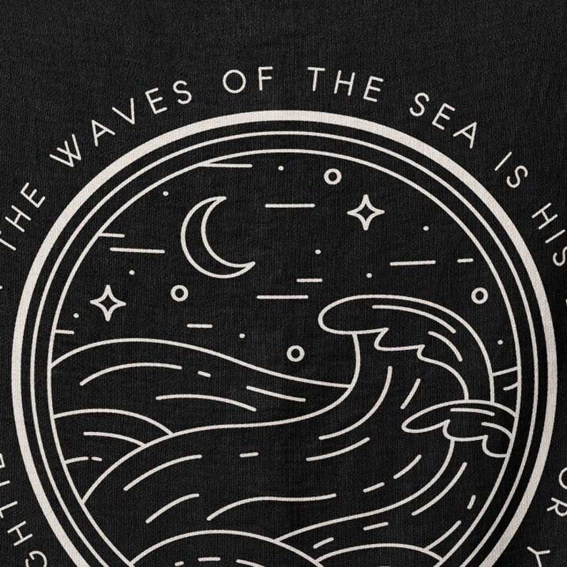 Op de afbeelding: Zwart grafisch ontwerp met een cirkelvormige illustratie van oceaangolven, een halve maan, sterren en de tekst "THE WAVES OF THE SEA IS HIS STORY". Het ontwerp is in wit op een zwarte achtergrond, wat een opvallend contrast cre&euml;ert.