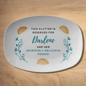 May include: White oval serving platter with the text "THIS PLATTER IS RESERVED FOR Darlene AND HER INCREDIBLY DELICIOUS PIEROGI". Features illustrations of pierogi and teal floral designs.