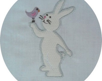 May include: A white embroidered bunny with a pink bird on a light blue background.