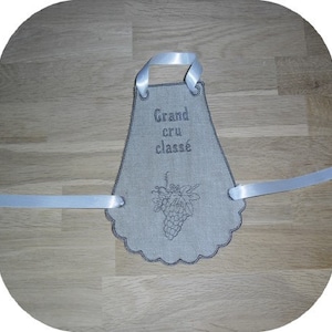 May include: A white linen kitchen towel with a scalloped edge and a white ribbon loop. The towel is embroidered with the text "Grand cru classé" and a bunch of grapes.