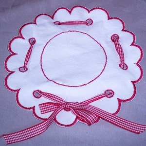 May include: White scalloped fabric circle with red and white gingham ribbon tied in a bow. The fabric circle has holes around the edge and the ribbon is threaded through the holes.