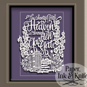 May include: White paper cut art framed in a brown frame. The art depicts a garden gate with flowers and the text "The shortest path to Heaven is through the garden gate". The bottom right corner of the frame has the text "Paper, Ink & Knife".
