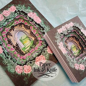 May include: Two paper art pieces featuring a layered design of a garden archway, surrounded by pink roses and green foliage. The artwork has a dark brown background. The text "Paper, Ink & Knife" is visible in the lower right corner.