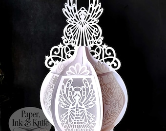 May include: White papercraft ornament shaped like a lantern with an angel design. The ornament is made of intricate cut-out paper and has a delicate, ethereal look.