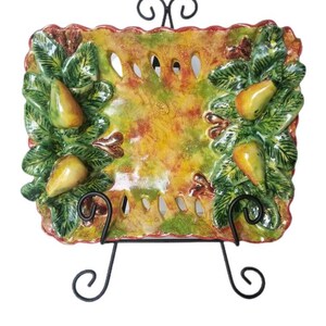 May include: A ceramic serving dish with a green, yellow, and red glaze. The dish is decorated with pears and leaves. It is on a black metal stand.