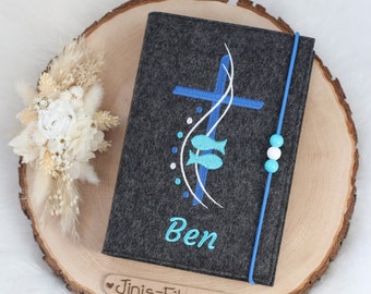 May include: Gray felt book cover with a blue cross, two blue fish, and white waves. The name "Ben" is embroidered in blue below the cross. The cover has a blue ribbon with white and blue beads.