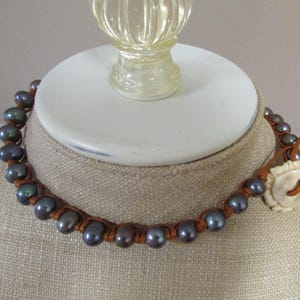 May include: A brown leather necklace with dark blue pearls and a white bone button accent.