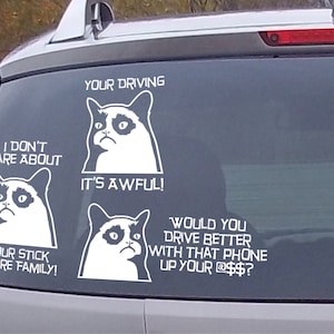 Może przedstawiać: Biała naklejka z Grumpy Catem na tylnej szybie samochodu. Naklejka głosi "Your Driving. I Don't Care About Your Stick Figure Family! It's Awful!" i "Would You Drive Better With That Phone Up Your @$$?"