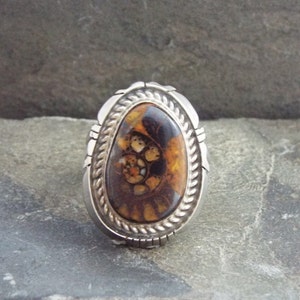 May include: A silver ring with a brown and white oval gemstone. The gemstone has a swirling pattern.