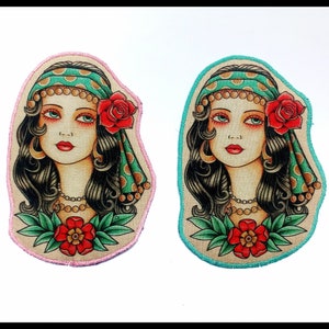 May include: Two embroidered patches featuring a vintage-style portrait of a woman with long black hair, a headscarf, and a red rose. One patch has a pink border, the other has a teal border. Both have a red flower at the bottom.