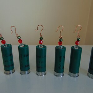 May include: Six green shotgun shell earrings with red and green beads. The shells are labeled with different gauges and sizes.