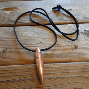 May include: A copper-colored bullet pendant on a black leather cord necklace.