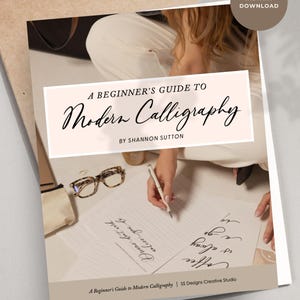 Könnte beinhalten: Ein Anfängerleitfaden für moderne Kalligraphie von Shannon Sutton, sofortiger Download. Das Bild zeigt eine Person, die Kalligraphie mit einem Stift schreibt. Das Buchcover ist hellrosa mit schwarzem Text. Eine Brille und eine kleine Tasche liegen auf dem Tisch.