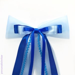 Könnte beinhalten: Eine blaue und hellblaue Schleife mit einem Tüllschwanz. Die Schleife ist mit einem Satinband gebunden und hat einen gewellten Rand.