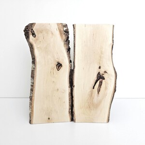 Könnte beinhalten: Zwei natürliche Holzscheiben mit Rindenkanten, jede mit einem einzigartigen Maserungsmuster und Knoten. Das Holz ist hellbraun und hat eine glatte Oberfläche.