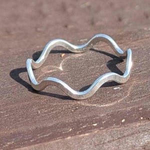 May include: A silver ring with a wavy design. The ring has an irregular, flowing shape and is made of a shiny metal. The ring is a piece of jewellery.