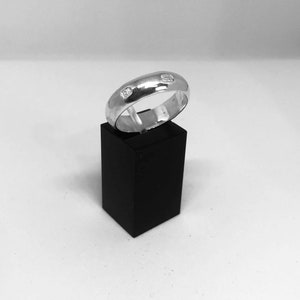 Pode incluir: Um anel de banda de prata com três pequenas pedras preciosas transparentes engastadas na banda.