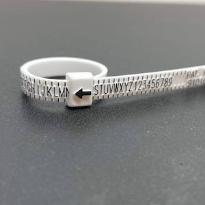 May include: White plastic ring sizer with a black arrow and markings for sizing. The markings include letters A through Z and numbers 1 through 9. The text "PAT. PEND. 9101681" is printed on the sizer.