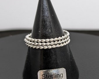 May include: Three silver rings stacked on a black ring display stand. The stand has a label that reads "Sterling Silver".