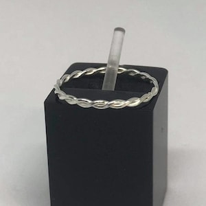 May include: A silver twisted ring on a black display stand.