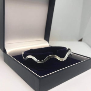 May include: A silver wavy bangle bracelet in a black velvet lined box.