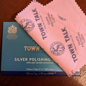 May include: A pink silver polishing cloth with the text "Town Talk - Polish Co Ltd" and "Silver Polishing Cloth". The cloth is folded in half and is sitting on top of a blue box with the text "Town Talk - Polish Co Ltd" and "Silver Polishing Cloth with anti-tarnish protection".