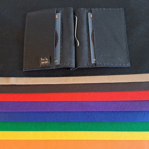 May include: A black leather wallet with a money clip and the text "Rexy Designs" on the front. The wallet is on a black surface with a rainbow of fabric swatches below it.