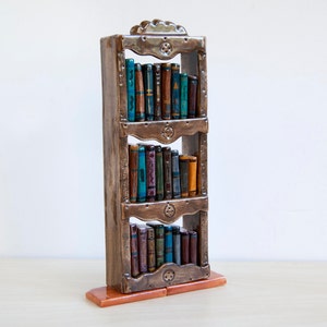 May include: A decorative ceramic bookshelf with three shelves, filled with miniature books. The bookshelf is brown with ornate detailing, and the books have colorful spines. The base is a reddish-brown color.