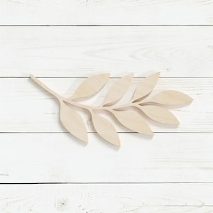 May include: A wooden branch with leaves cut out, painted in a light brown color, against a white wood background.