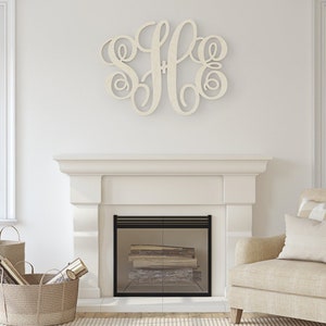 May include: A white wooden monogram with the letters "SFE" in a cursive script style. The monogram is hanging on a white wall above a fireplace.