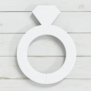 May include: White wooden ring with a diamond shape on top. The ring is on a white wood background.