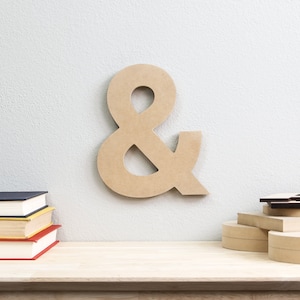 May include: A large, wooden ampersand symbol, painted in a light brown color, is mounted on a white wall. The ampersand is a decorative element for a home or office.