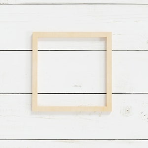 May include: A simple, light wood picture frame on a white wood background.