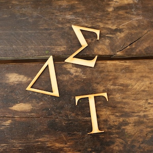 May include: Three wooden letters, a triangle, a T, and a sigma, are arranged on a brown wooden surface.