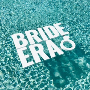 May include: White letters spelling "Bride Era" floating in a turquoise blue swimming pool.