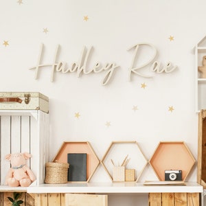 May include: A white wooden sign with the name "Hadley Rae" in cursive script. The sign is mounted on a white wall with gold stars.