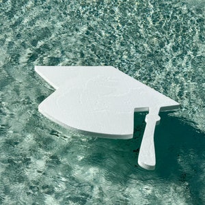 May include: A white graduation cap shape floating in a blue pool of water.