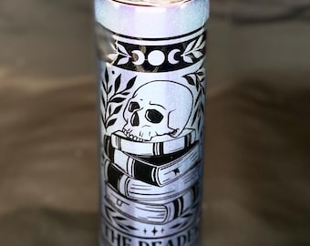 May include: A light blue tumbler with a clear lid. The tumbler features a black graphic of a skull atop a stack of books, with the words "THE READER" at the bottom. The design includes crescent moons and leaves.