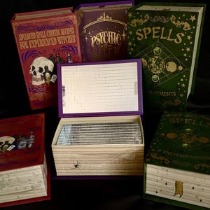 May include: A collection of five decorative book-shaped boxes. Three are closed, featuring titles like Advanced Spell Casting Recipes for Experienced Witches, Psychic, and Spells. Two are open, revealing a mirrored interior and a spider web design.