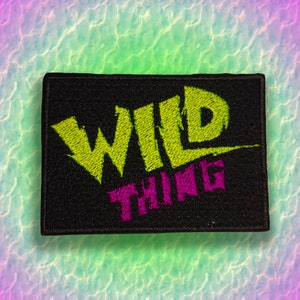 May include: A black embroidered patch with the words "WILD THING" in yellow and pink lettering.