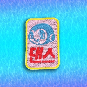 May include: A pink and yellow embroidered patch with a blue cartoon character and the Korean text "댄스" in red.