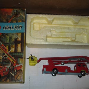 May include: A red fire truck toy with a ladder extension and a yellow bucket on the end. The toy is in its original box, which has a picture of the truck in action and the words "Corgi Toys Major" on the front.