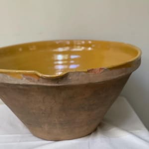 May include: A large, yellow glazed earthenware bowl with a brown clay base. The bowl has a chipped rim and is slightly misshapen.
