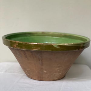 May include: A terracotta planter with a green glazed rim. The planter is a traditional style with a wide base and a narrow opening.