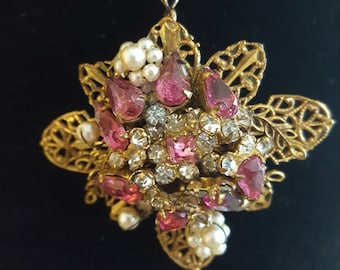 May include: A gold-tone pendant featuring a cluster of pink and clear rhinestones, surrounded by faux pearls, set in a delicate filigree design.