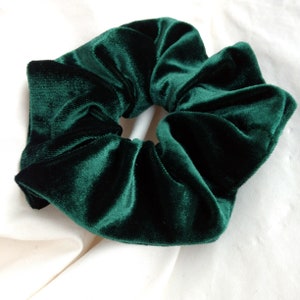 Puede incluir: Una goma para el pelo de terciopelo verde esmeralda oscuro. La tela es suave y afelpada, con textura y pliegues visibles. La goma es un accesorio para el cabello, dise&ntilde;ado para sujetar el pelo en una coleta o mo&ntilde;o.