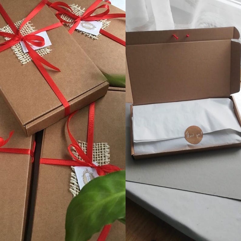 Puede incluir: Varias cajas de cart&oacute;n marr&oacute;n atadas con cinta roja y detalles de arpillera. Una caja est&aacute; abierta, revelando papel de seda blanco y una pegatina redonda que dice "Thank you!". Las cajas son probablemente para regalos o embalaje.